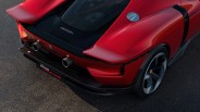 Rear view of a red Ferrari SF90 Stradale showing the dual exhaust pipes, rear spoiler, fuel cap, rear wheel with five-spoke rim, and the Ferrari logo on the back. The car is parked on an asphalt surface.