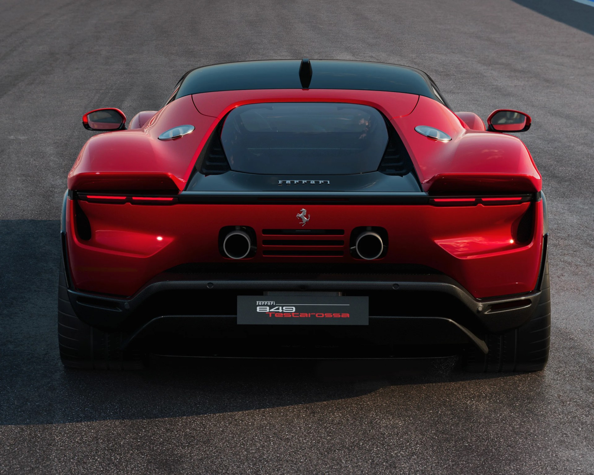 Rear view of a red Ferrari 849 Testarossa with a black roof, dual exhaust pipes, and sleek taillights, parked on a paved surface.