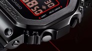 Close-up of a black Casio G-Shock digital watch showing part of the display with red accents, the metal bezel with "G-SHOCK" engraved, and side buttons. The watch has a rugged, matte finish with visible screws and a sturdy design.