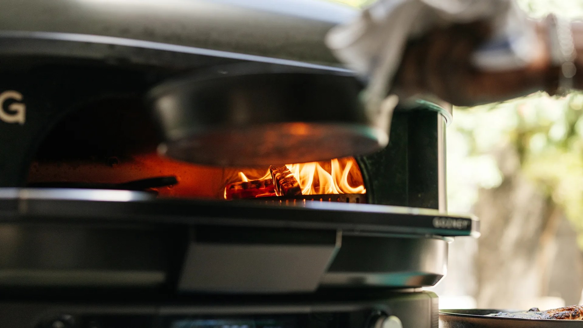 Close-up of a wood-fired oven with visible flames and glowing embers inside, showing the heat source used for cooking.