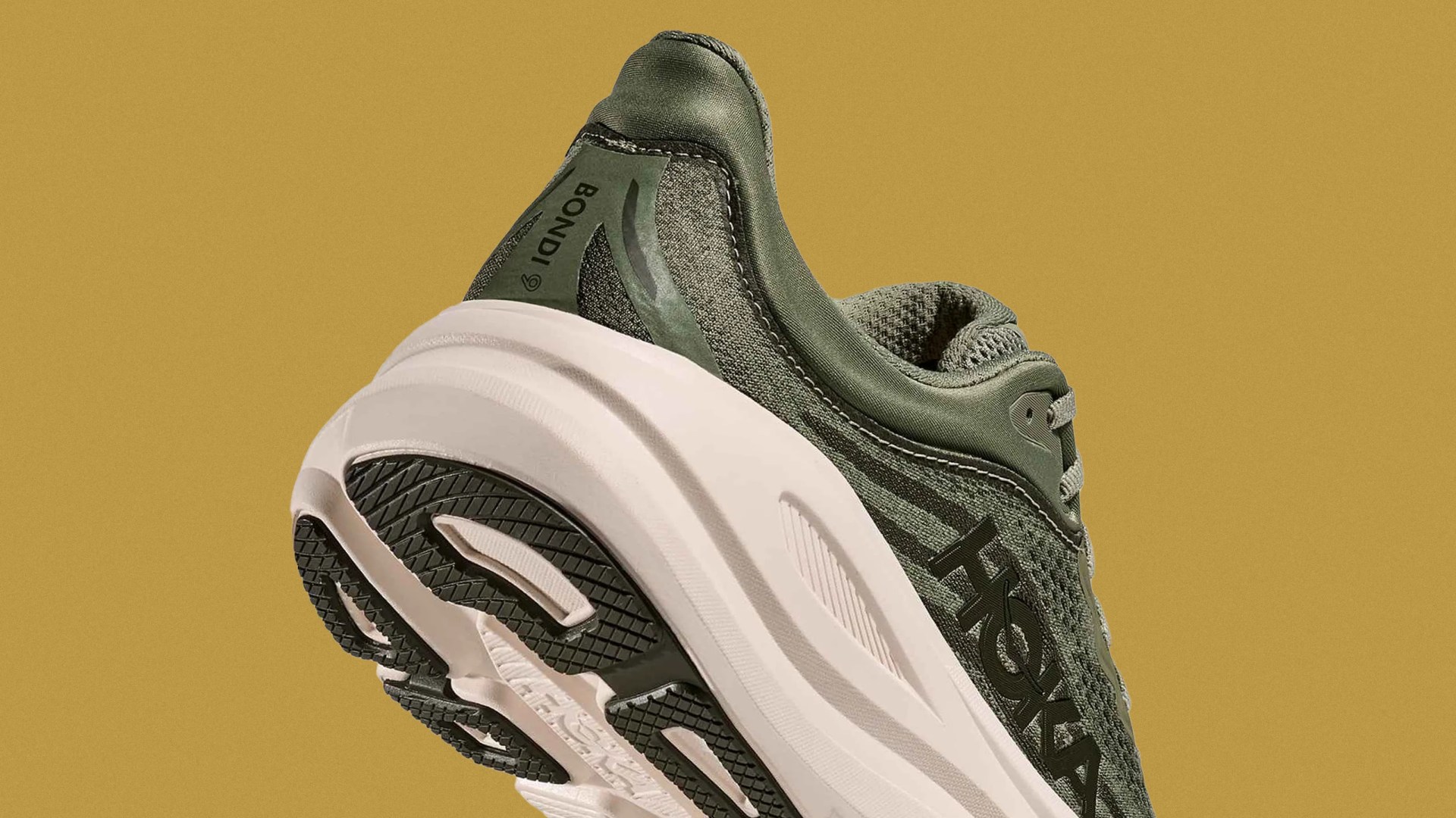 Green Hoka Bondi 6 running shoe with a thick white sole and black tread, shown from a low rear angle against a mustard yellow background.