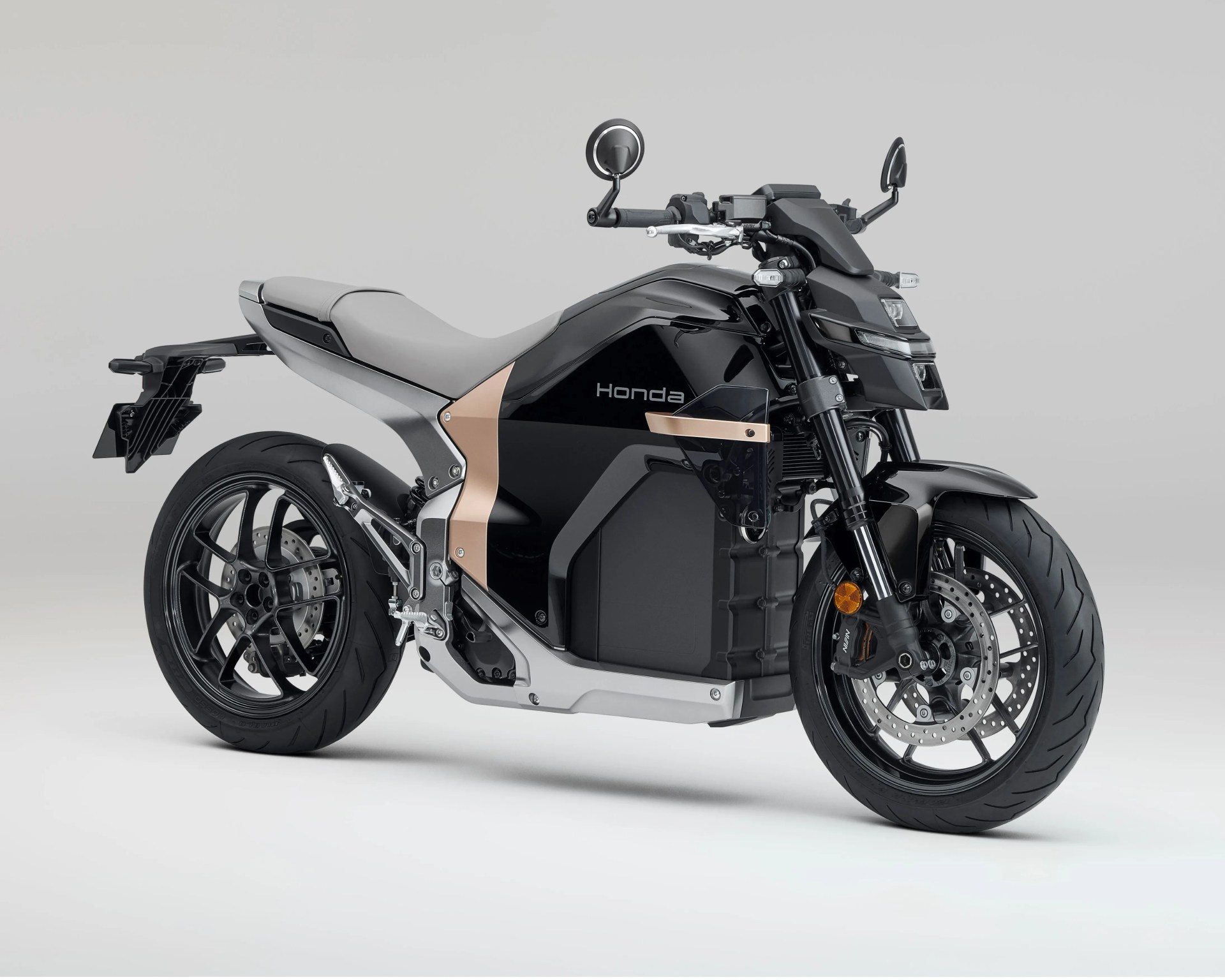 A sleek black and gray Honda electric motorcycle with a modern, angular design. It features a matte gray seat, black wheels with disc brakes, and a compact, streamlined body with subtle bronze accents. The bike has round rearview mirrors and a distinctive front headlight assembly.