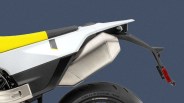 Rear section of a motorcycle featuring a yellow and white seat, a large silver exhaust pipe, and a black rear fender with a red reflector. The rear tire is partially visible below. The background is a solid dark blue.