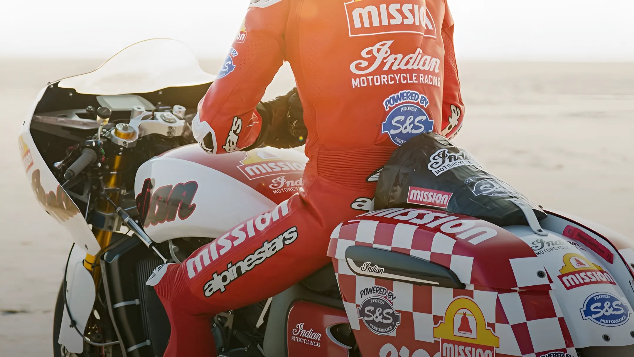 Rider in red racing suit sitting on a white and red Indian Motorcycle with Mission and S&S logos.