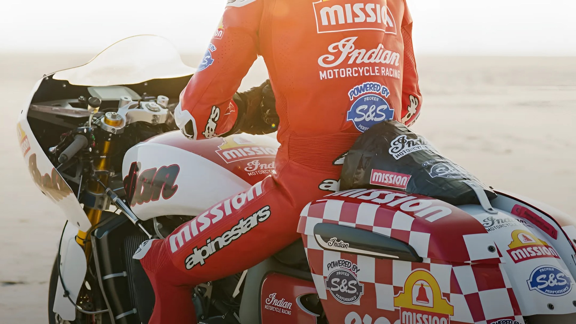 Rider in red racing suit sitting on a white and red Indian Motorcycle with Mission and S&S logos.