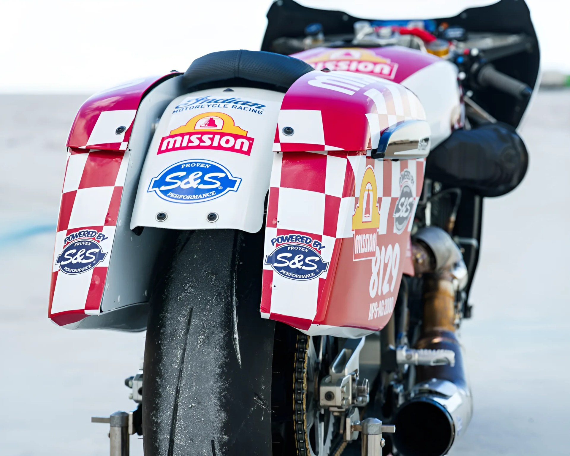 Rear view of a red and white checkered racing motorcycle with "Mission" and "S&S" logos on the rear fender and tire.