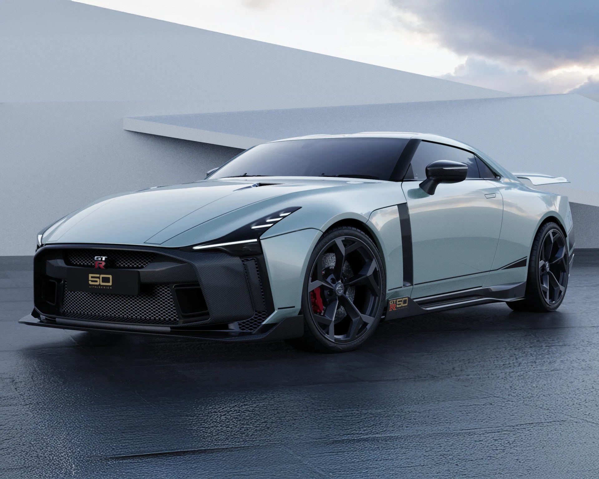 Sleek silver Nissan GT-R 50 Italdesign sports car with black accents, aggressive front grille, sharp LED headlights, large black alloy wheels, and a rear spoiler, parked on a textured dark surface against a modern minimalist backdrop.