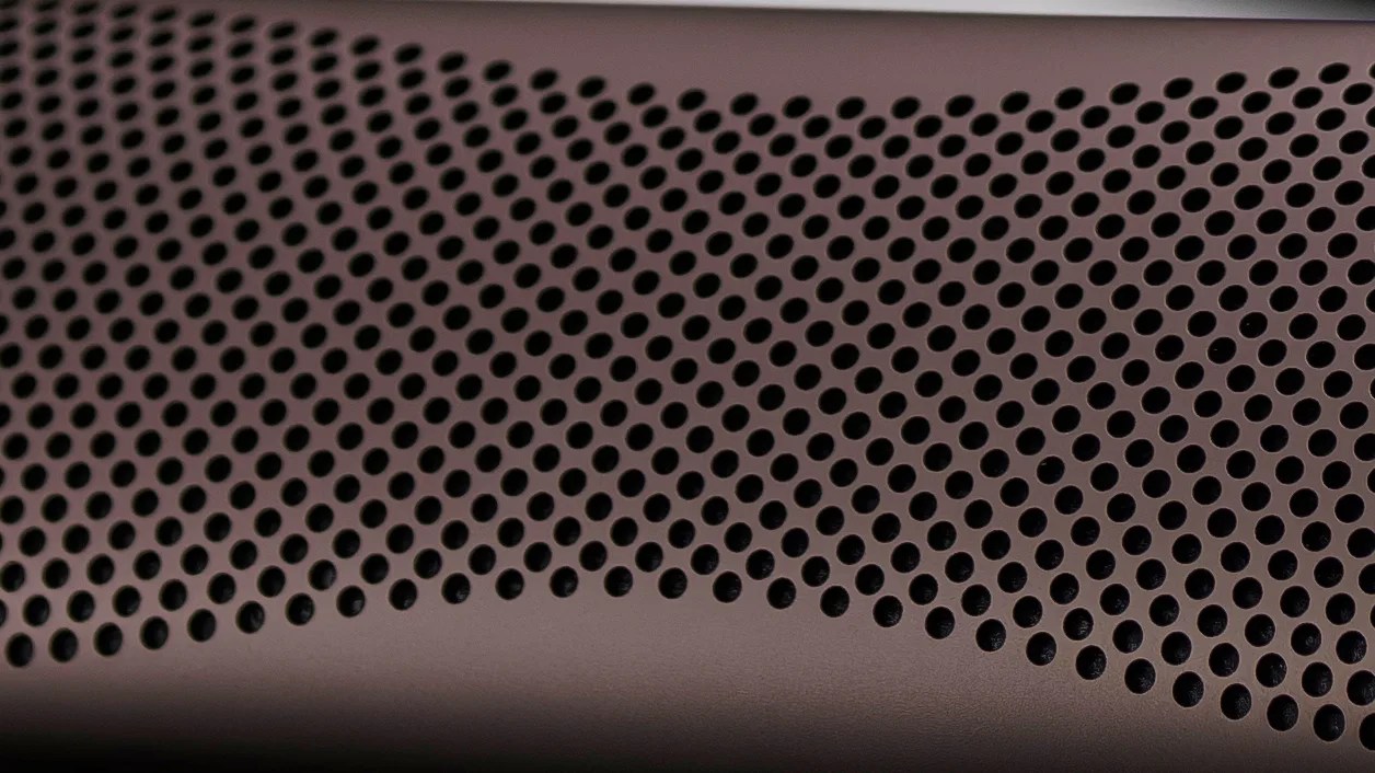 Close-up of a brown surface with a pattern of evenly spaced circular holes, likely a speaker grille or ventilation panel.