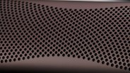 Close-up of a brown surface with a pattern of evenly spaced circular holes, likely a speaker grille or ventilation panel.