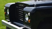 Front view of a black Land Rover vehicle, showing the grille with the "LAND-ROVER" badge, round headlights, and a silver front bumper, set against a green grassy background.