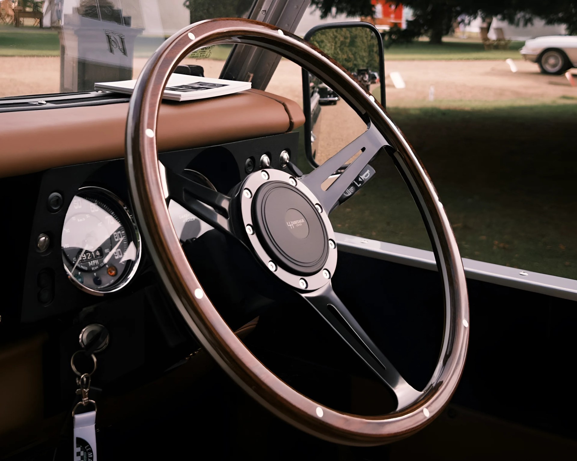 Wood-rimmed steering wheel with black metal spokes and a central hub labeled "Heritage 1948," set against a tan dashboard featuring a speedometer and ignition key with a white keychain.