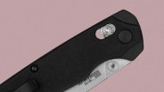 Close-up of a black folding knife handle with textured grip, showing a partially visible silver blade marked "610 USA" and metal screws near the pivot area.