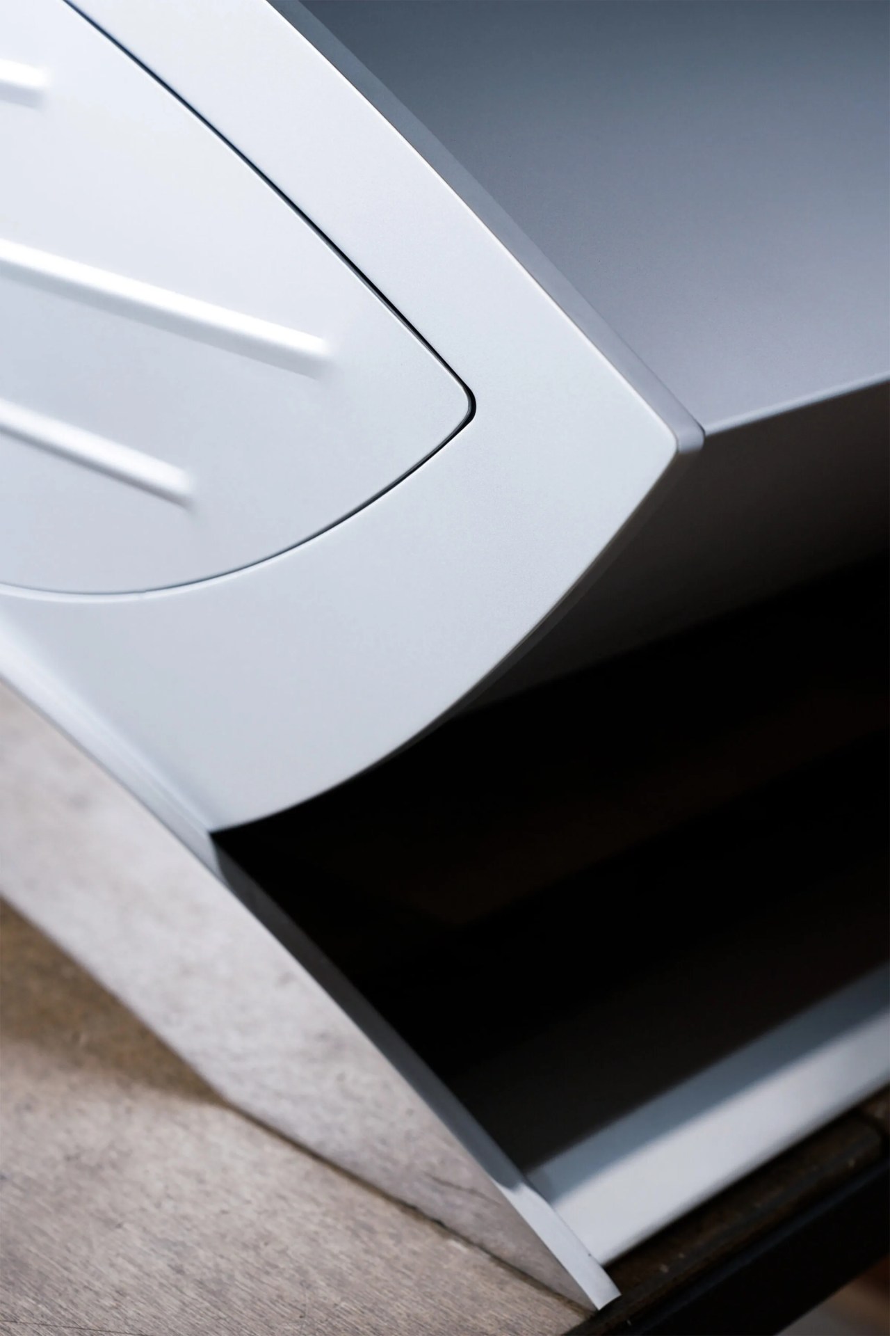 Close-up of a sleek, modern white and gray electronic device with a curved edge and a vent-like design on the white surface, resting on a wooden surface.
