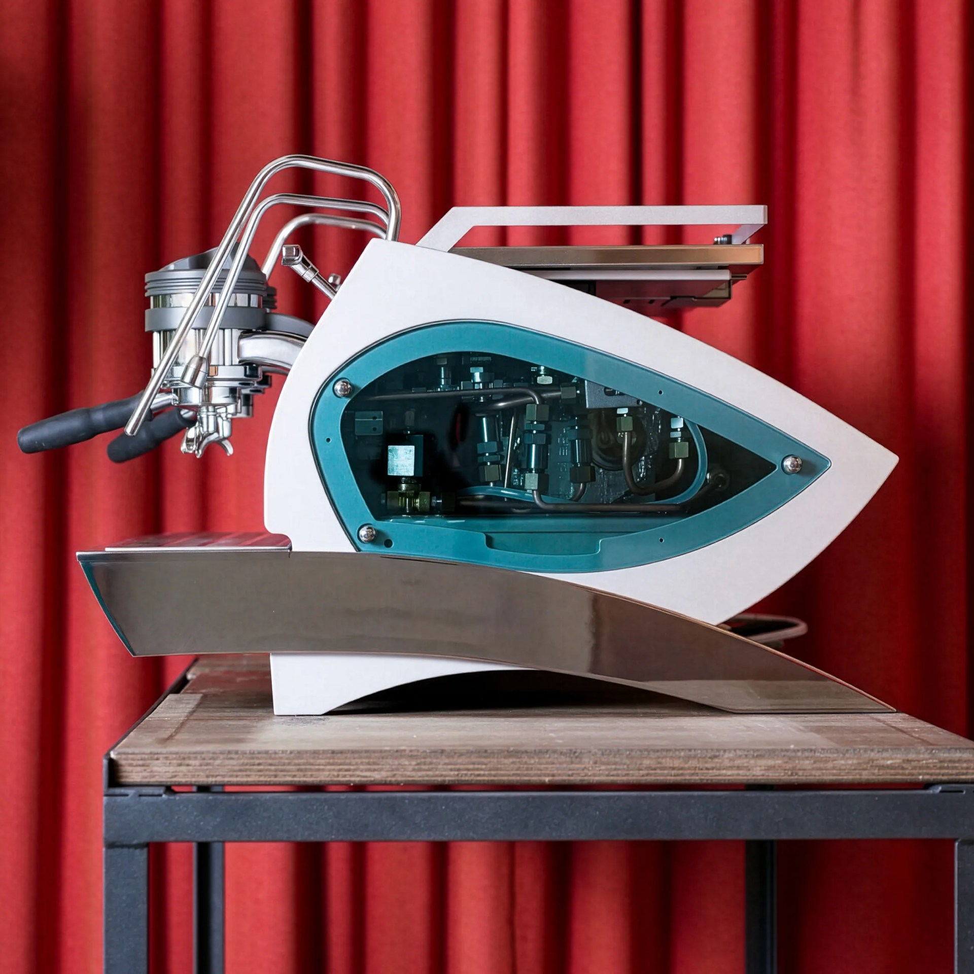 Close-up of a modern espresso machine group head with dual portafilters, chrome steam wands, and a partially visible internal mechanism through a blue-tinted window on the white machine body.