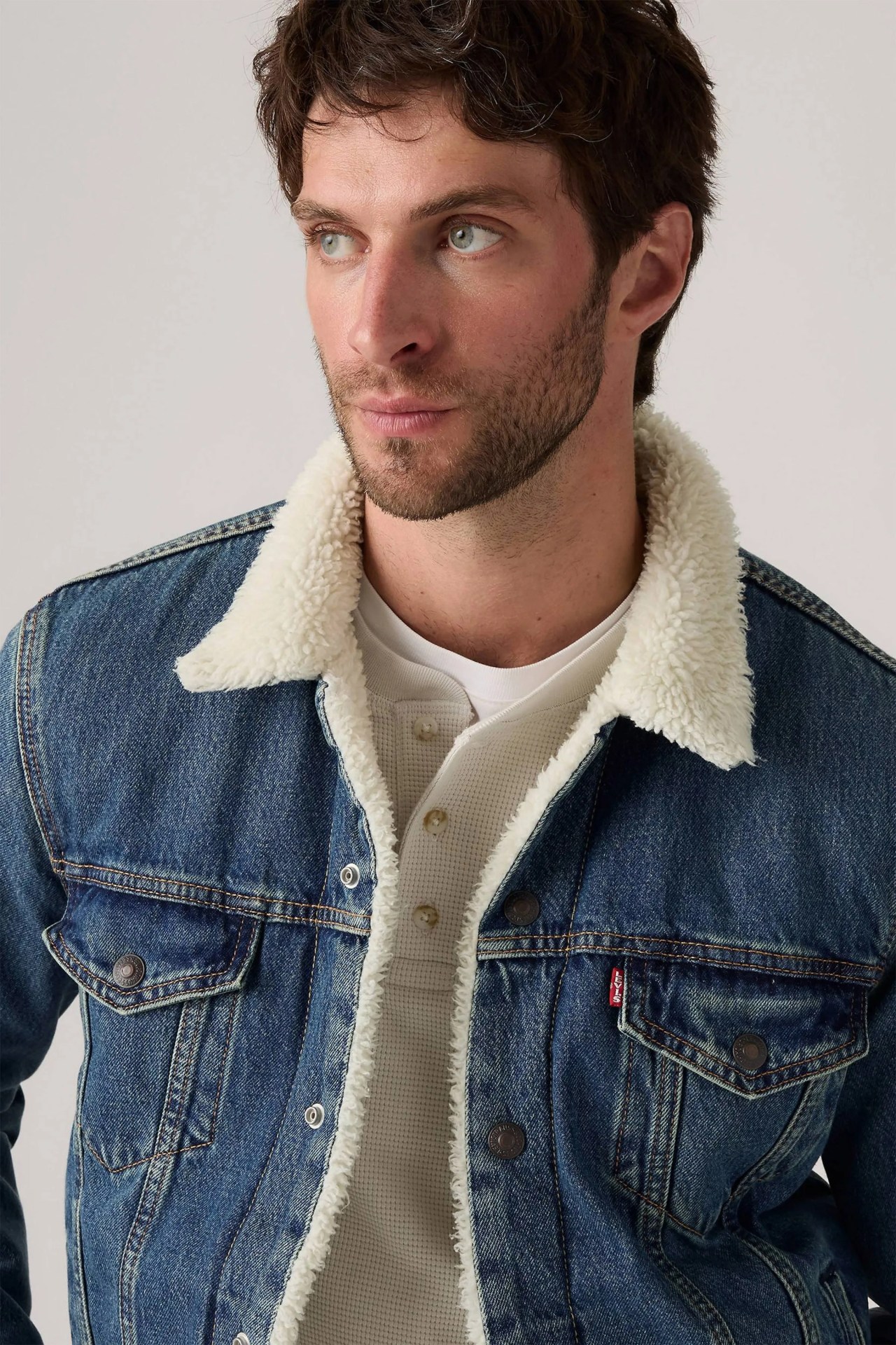 Man wearing a blue denim jacket with a white sherpa collar and lining, over a white waffle-knit henley shirt.