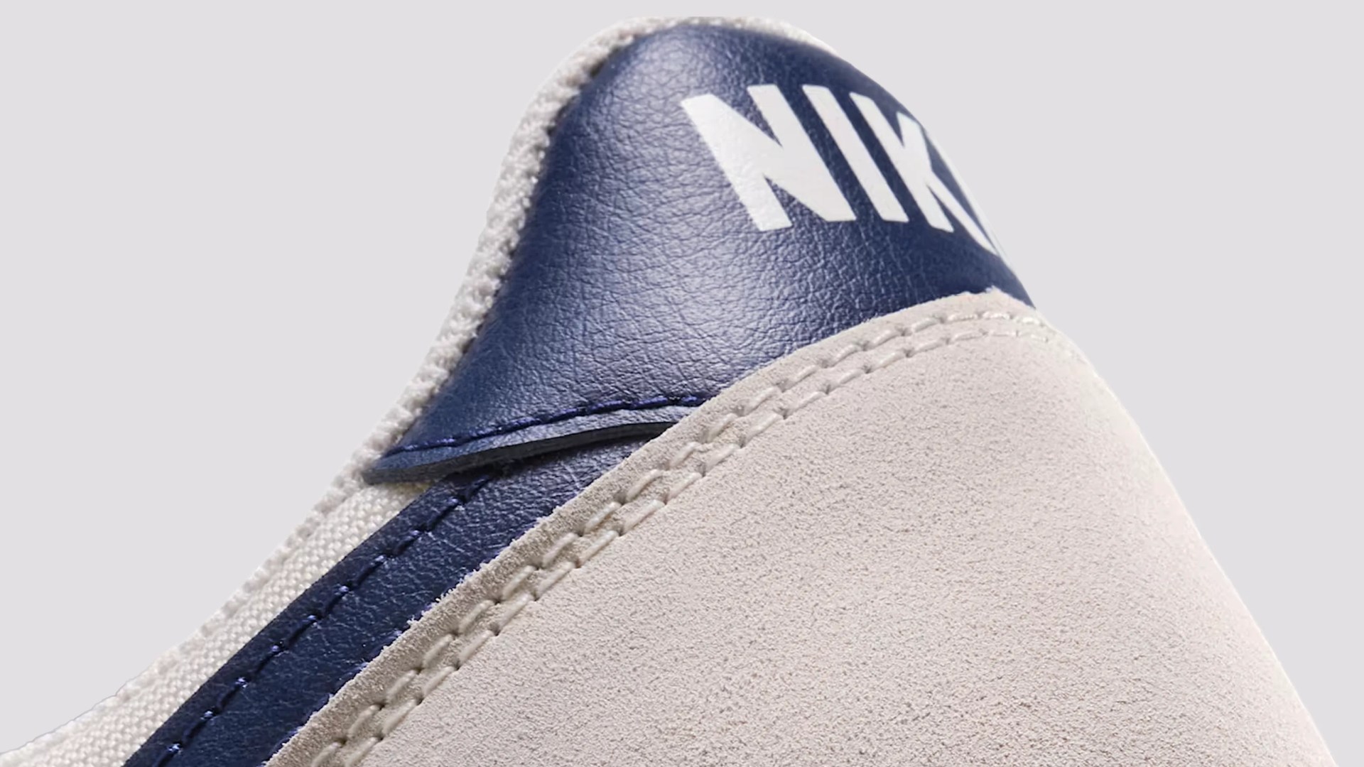 Close-up of the heel area of a Nike shoe, featuring a navy blue leather section with the white "NIKE" logo and light beige suede material with detailed stitching.