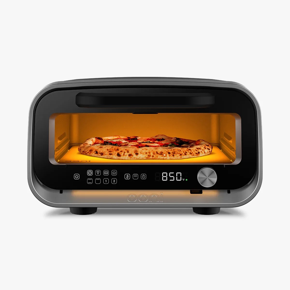 Countertop pizza oven with a digital display showing 850°F, a control knob, and touch buttons. Inside, a pizza is baking on a stone surface, illuminated by a warm orange light. The oven has a sleek, modern design with a black and silver finish.