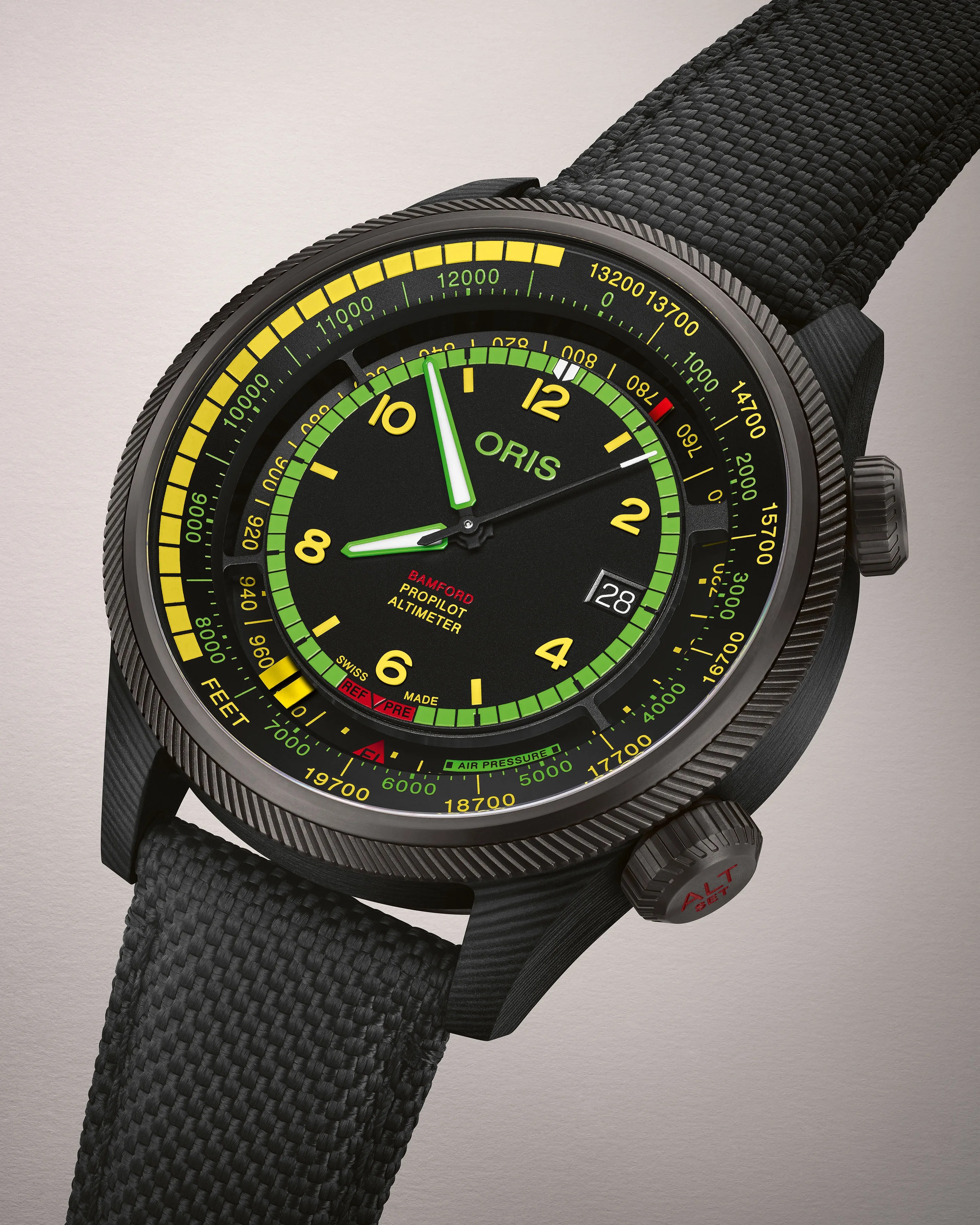Black Oris x Bamford ProPilot Altimeter watch with a textured black strap, featuring a black dial with yellow and green markings, luminous hands, a date window at 3 o'clock, and a knurled bezel and crown marked "ALT SET" in red.