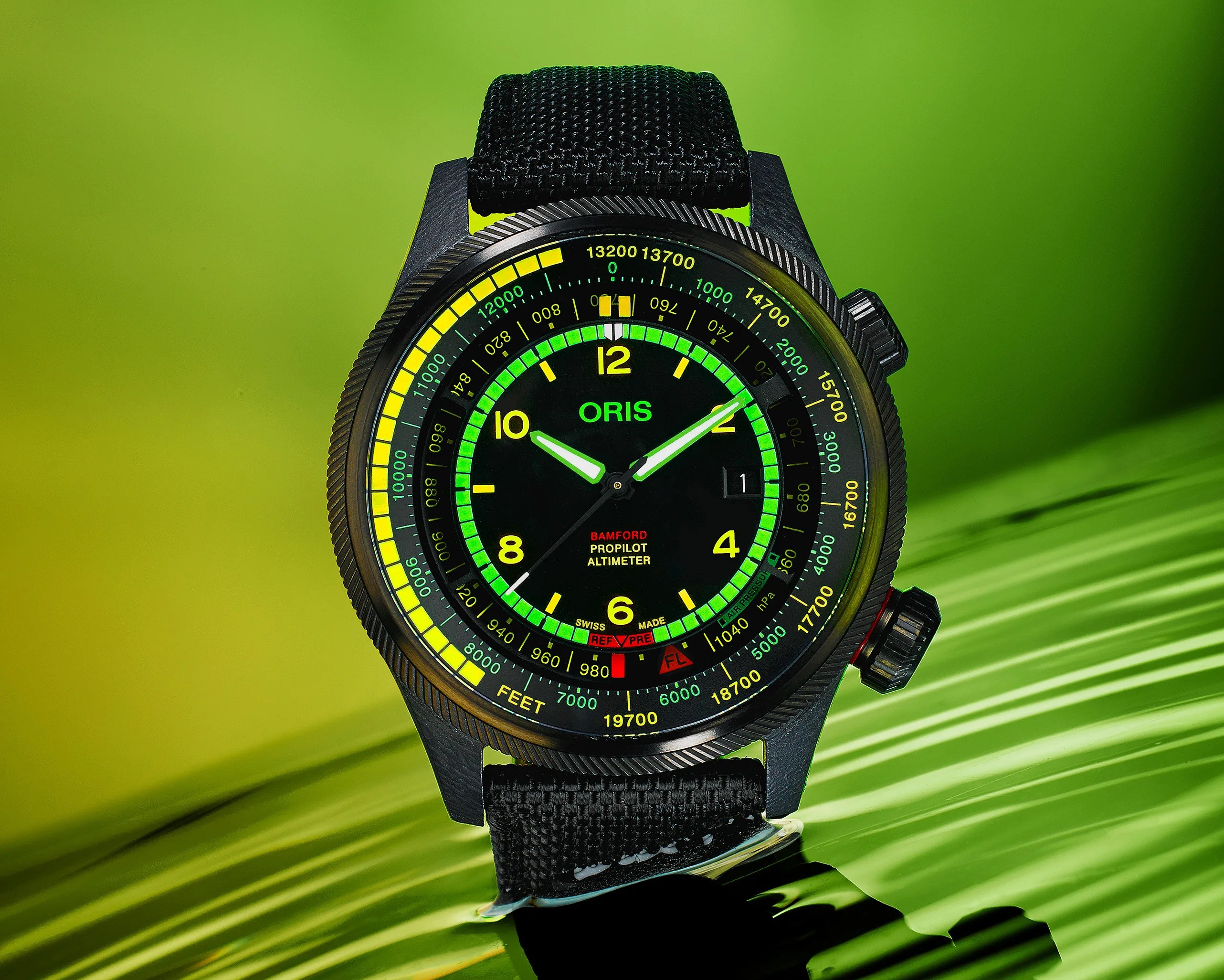 Black Oris ProPilot Altimeter watch with a black fabric strap, featuring a black dial with yellow and green markings, luminous hands, and a date window at 3 o'clock, set against a green gradient background.