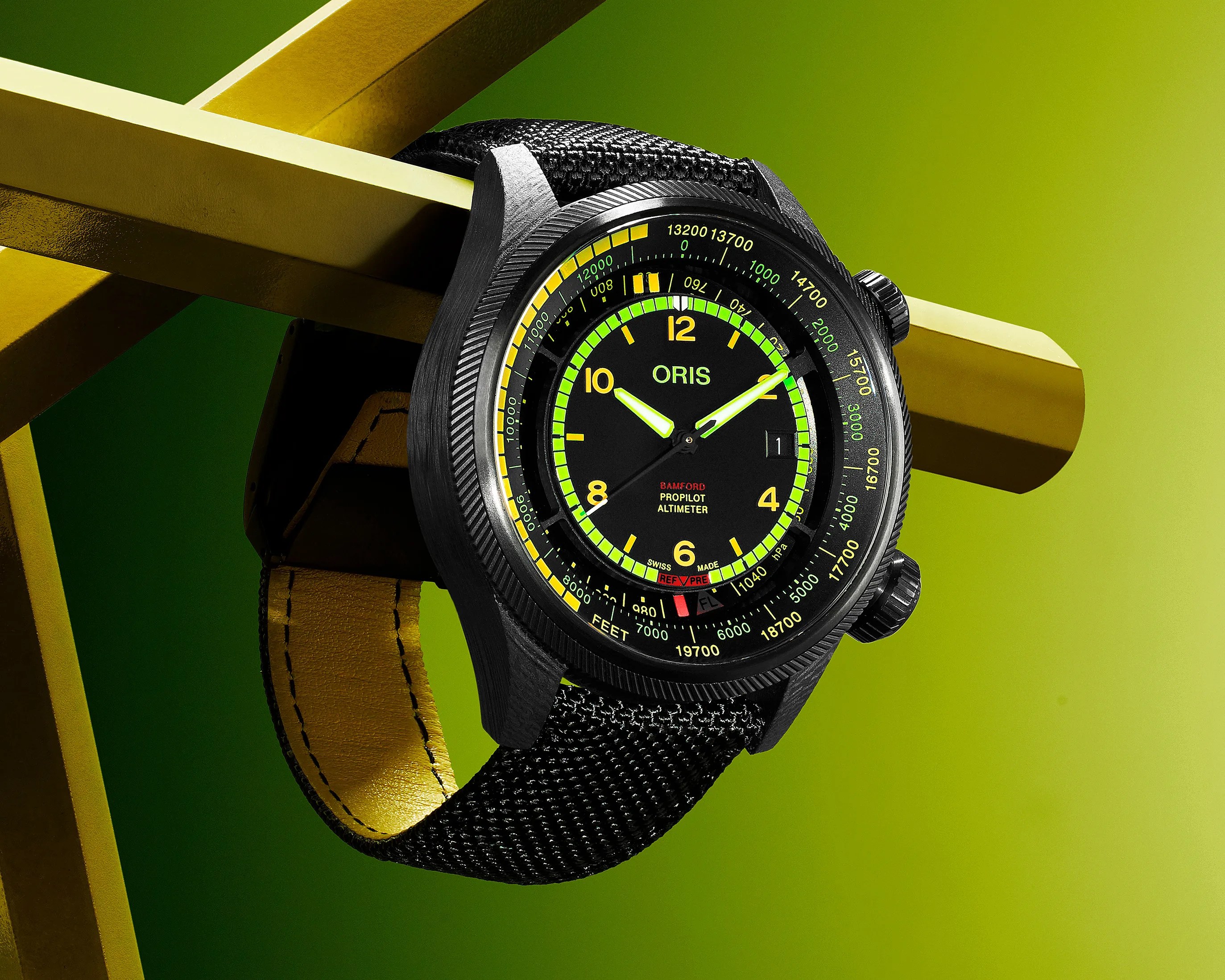 Black Oris ProPilot Altimeter wristwatch with yellow and green markings on the dial, featuring a black textured strap with yellow stitching on the inner side, displayed against a green background with a yellow geometric structure.