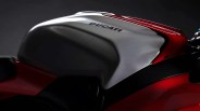 Close-up of a Ducati motorcycle fuel tank with a sleek, aerodynamic design. The tank is primarily silver with the Ducati logo in black and features red accents on the sides. The surface has a smooth, glossy finish with subtle reflections.