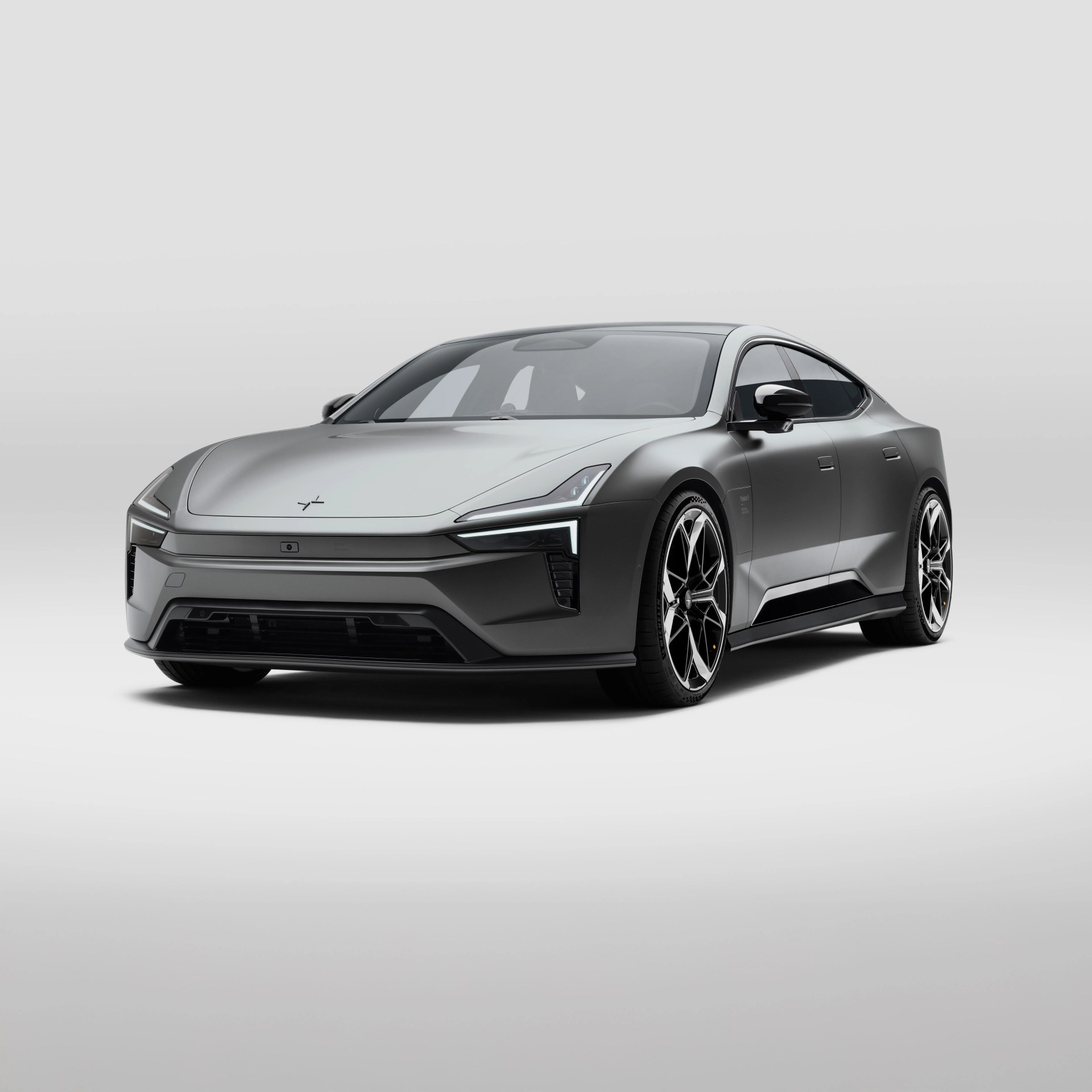 Sleek, modern electric sedan with a matte gray finish, sharp angular LED headlights, and large black and silver alloy wheels, shown from a front three-quarter view on a plain light gray background.
