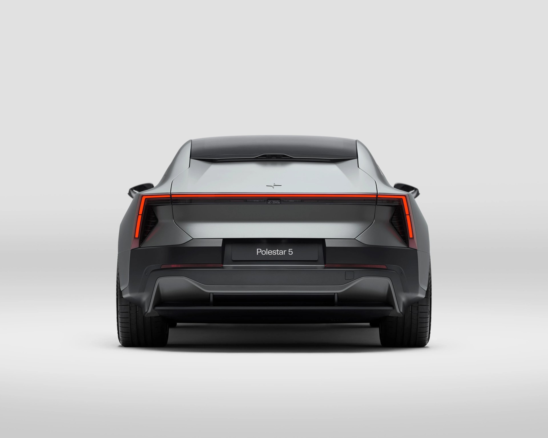 Rear view of a silver Polestar 5 electric car with a continuous horizontal red LED tail light strip and a black lower bumper against a plain light gray background.