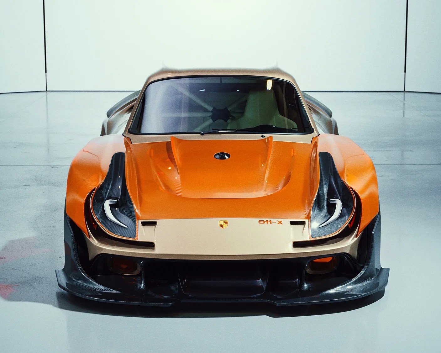Front view of a Porsche 911-X with a wide body kit, featuring an orange and beige color scheme, carbon fiber accents on the fenders and front splitter, and a sleek aerodynamic design. The car is displayed in a clean, minimalistic indoor setting.