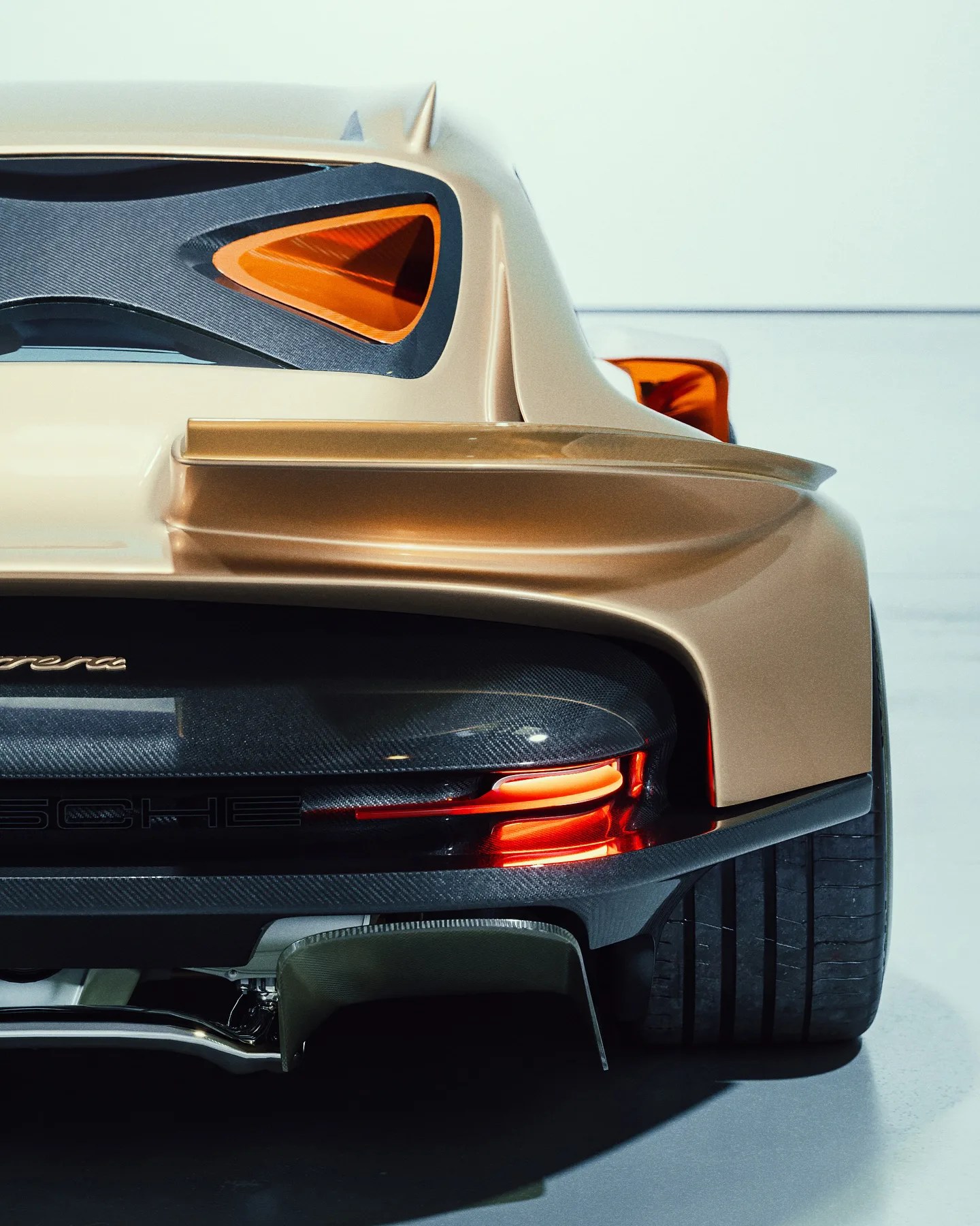 Rear view of a gold-colored Porsche Carrera, showcasing its sleek tail light design, wide rear tire, carbon fiber accents, and a prominent rear spoiler.