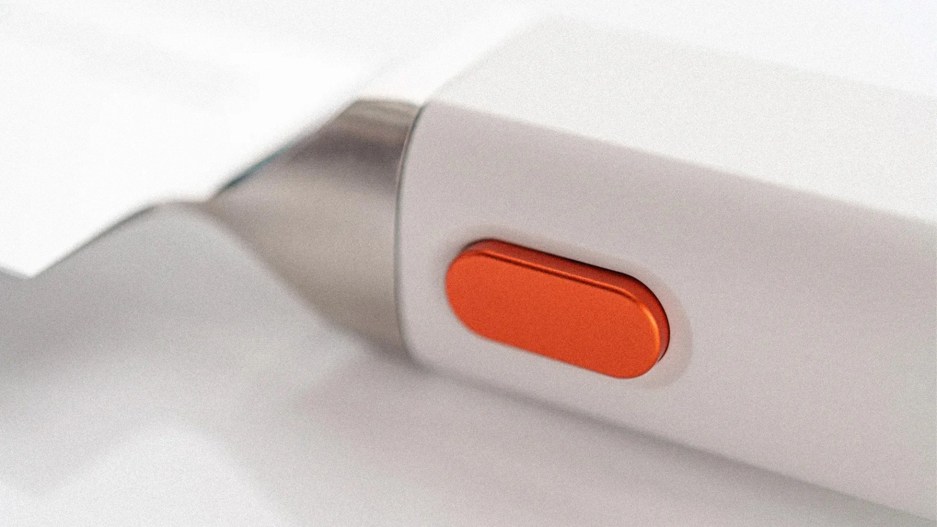 Close-up of a white electronic device with a metallic tip and an orange oval button on its side.