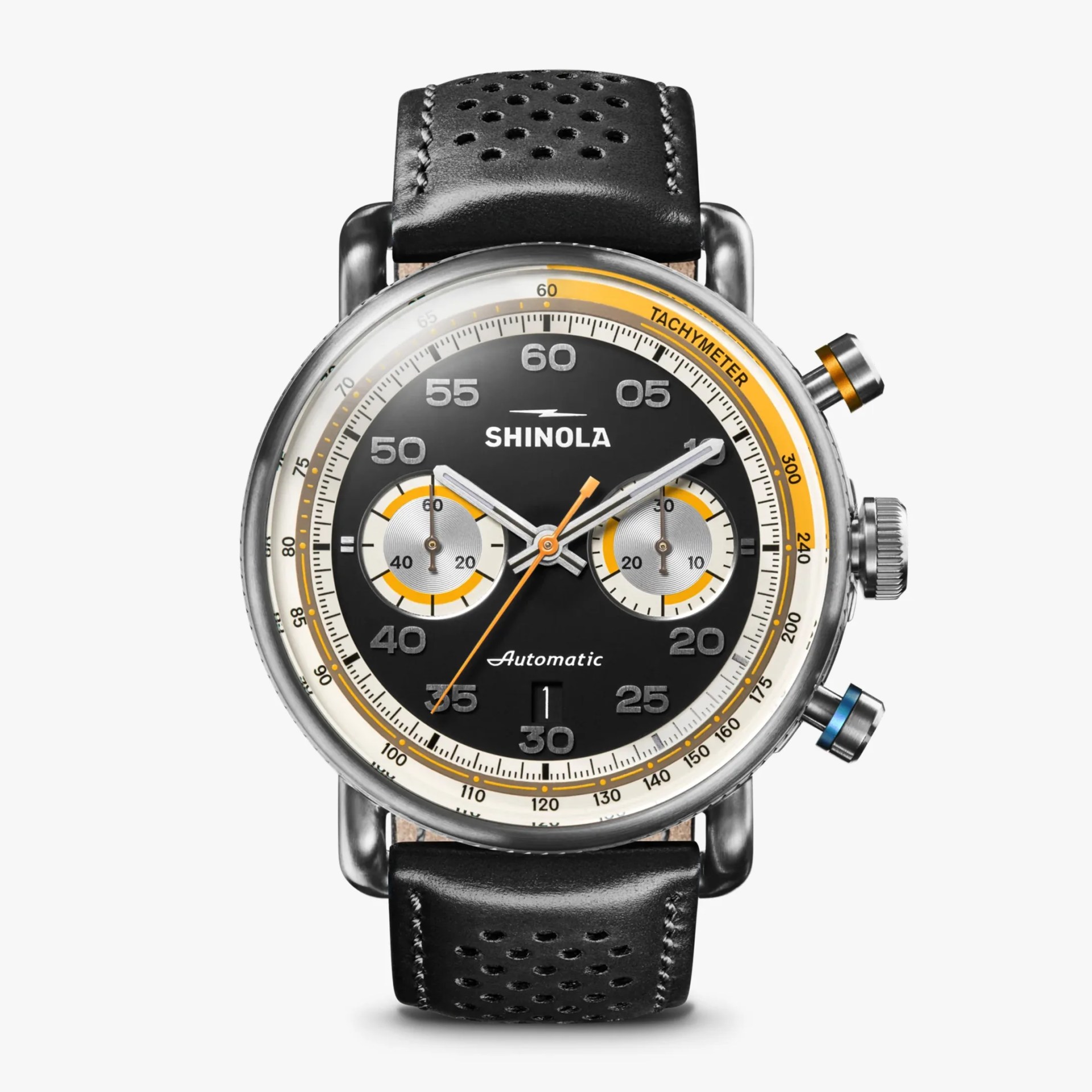 Black Shinola automatic chronograph watch with a round stainless steel case, black perforated leather strap, and a black dial featuring two silver subdials with yellow accents. The watch has silver hour markers and hands, an orange second hand, a date window at 6 o'clock, and a tachymeter scale on the outer edge. The chronograph pushers are accented with orange and blue.