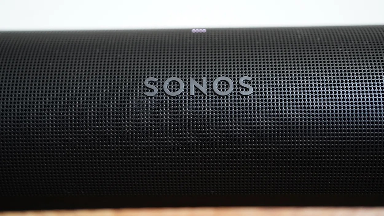 Close-up of a black Sonos speaker grille with the SONOS logo centered on the front. The grille has a pattern of small circular holes.