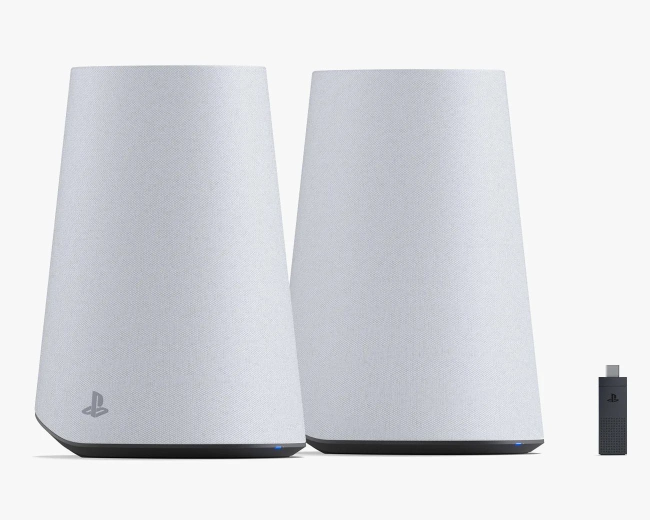 Two white PlayStation wireless speakers with a fabric texture and a small PlayStation logo on the lower front left of one speaker, accompanied by a small black USB dongle with a PlayStation logo. The speakers have a slightly tapered cylindrical shape with a black base and a small blue indicator light.
