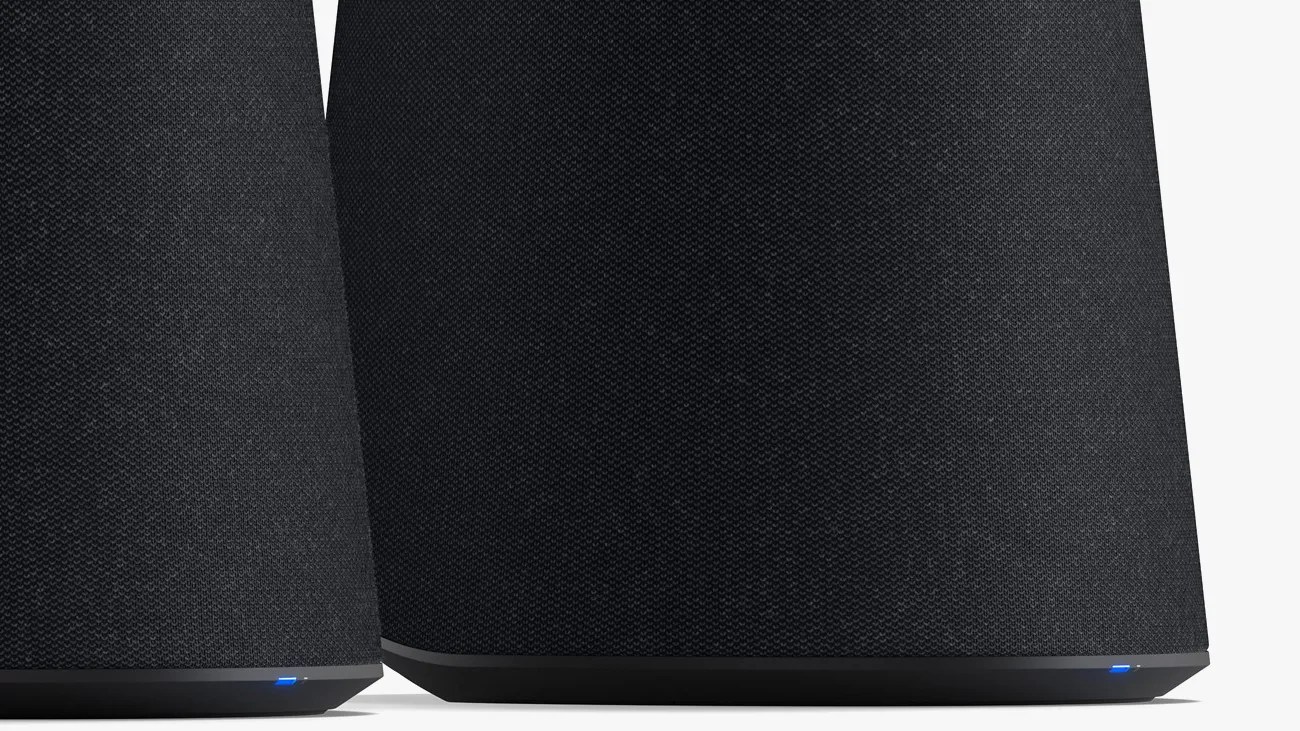 Two black fabric-covered speakers with a trapezoidal base, each featuring a small blue LED light near the bottom edge.