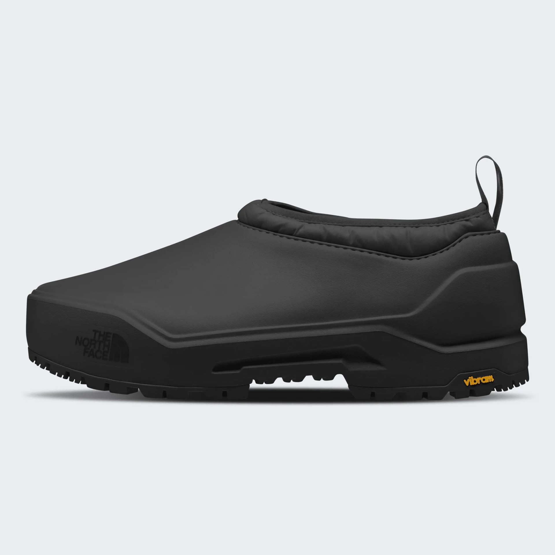 Black slip-on shoe with a smooth, matte finish and a padded collar. The shoe features a pull tab at the heel and a rugged sole with a Vibram logo in yellow near the heel. The North Face logo is subtly embossed on the front side of the sole.
