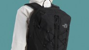 Black The North Face Borealis backpack with multiple compartments and adjustable straps, worn by a person in a white jacket against a teal background.