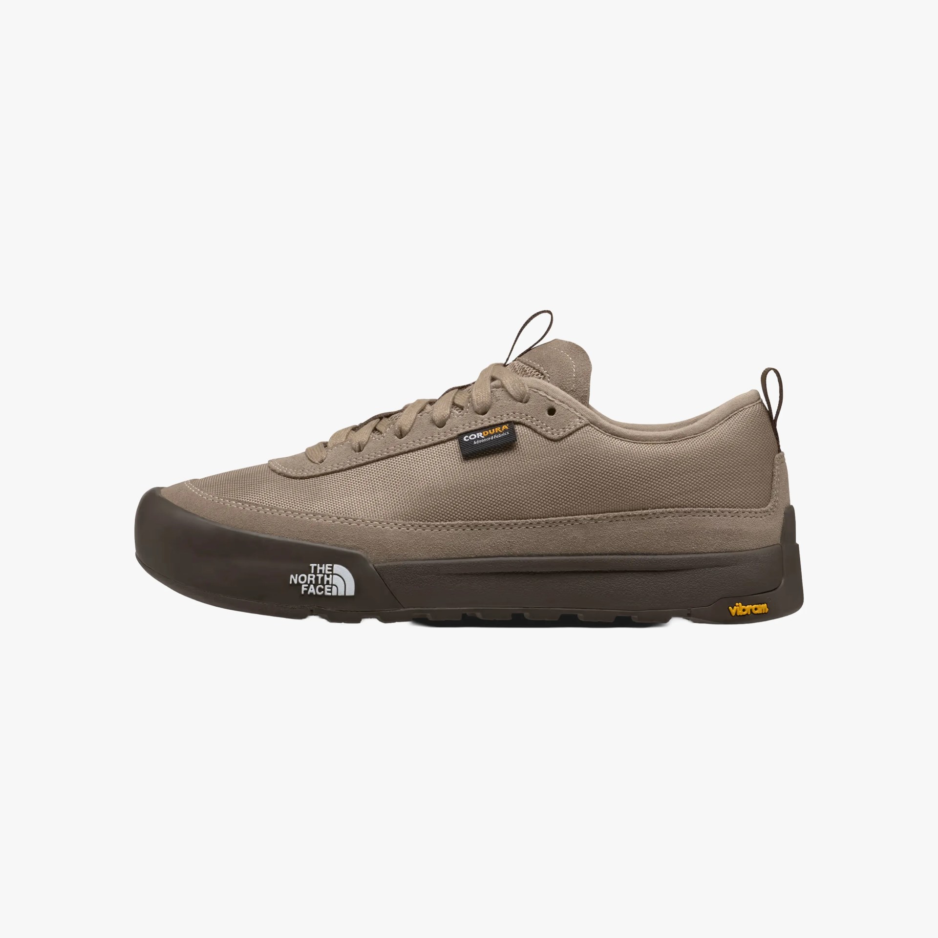 Low-top sneaker in taupe with a dark brown sole. The shoe features a lace-up design, a small black tag with "CORDURA" text on the side, and a pull tab at the heel and tongue. The sole has "THE NORTH FACE" logo in white near the toe and a yellow "vibram" logo near the heel. The upper material appears to be durable fabric.