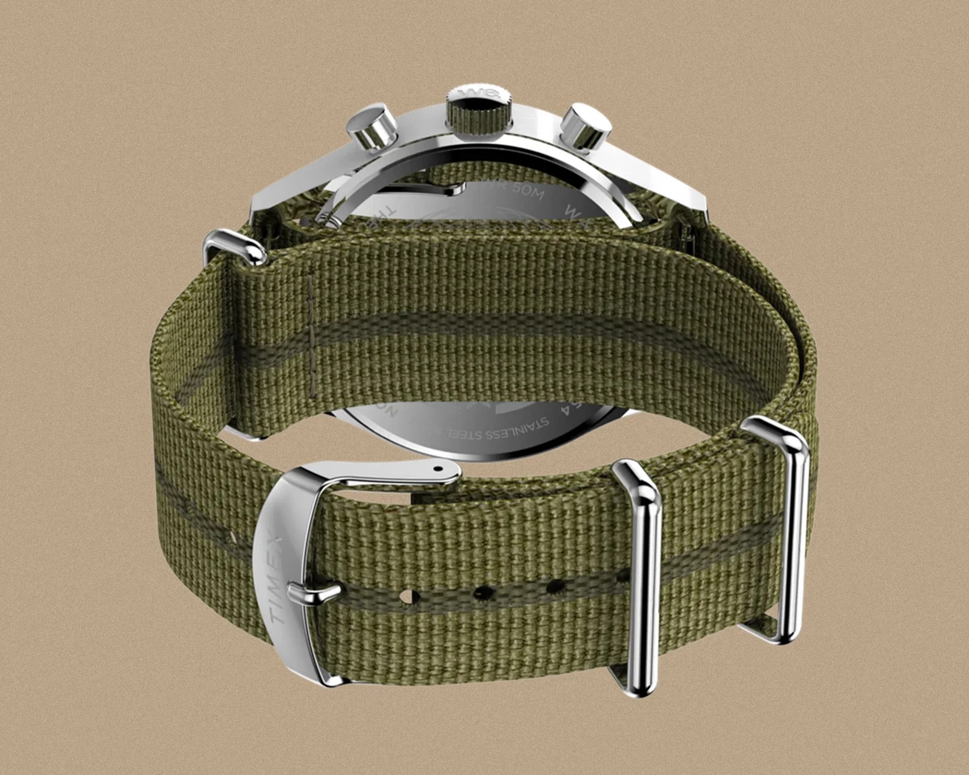 Green woven fabric watch strap with silver metal buckle and loops, attached to a silver watch case. The watch case back is visible, showing some engraved text. The strap has a subtle darker green stripe running through the middle.