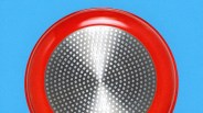 Bottom view of a red frying pan with a circular stainless steel base featuring a pattern of small raised dots, set against a blue background.