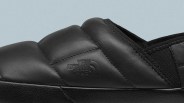 Close-up of a black padded shoe with "The North Face" logo embossed on the side, featuring detailed stitching and a textured sole.