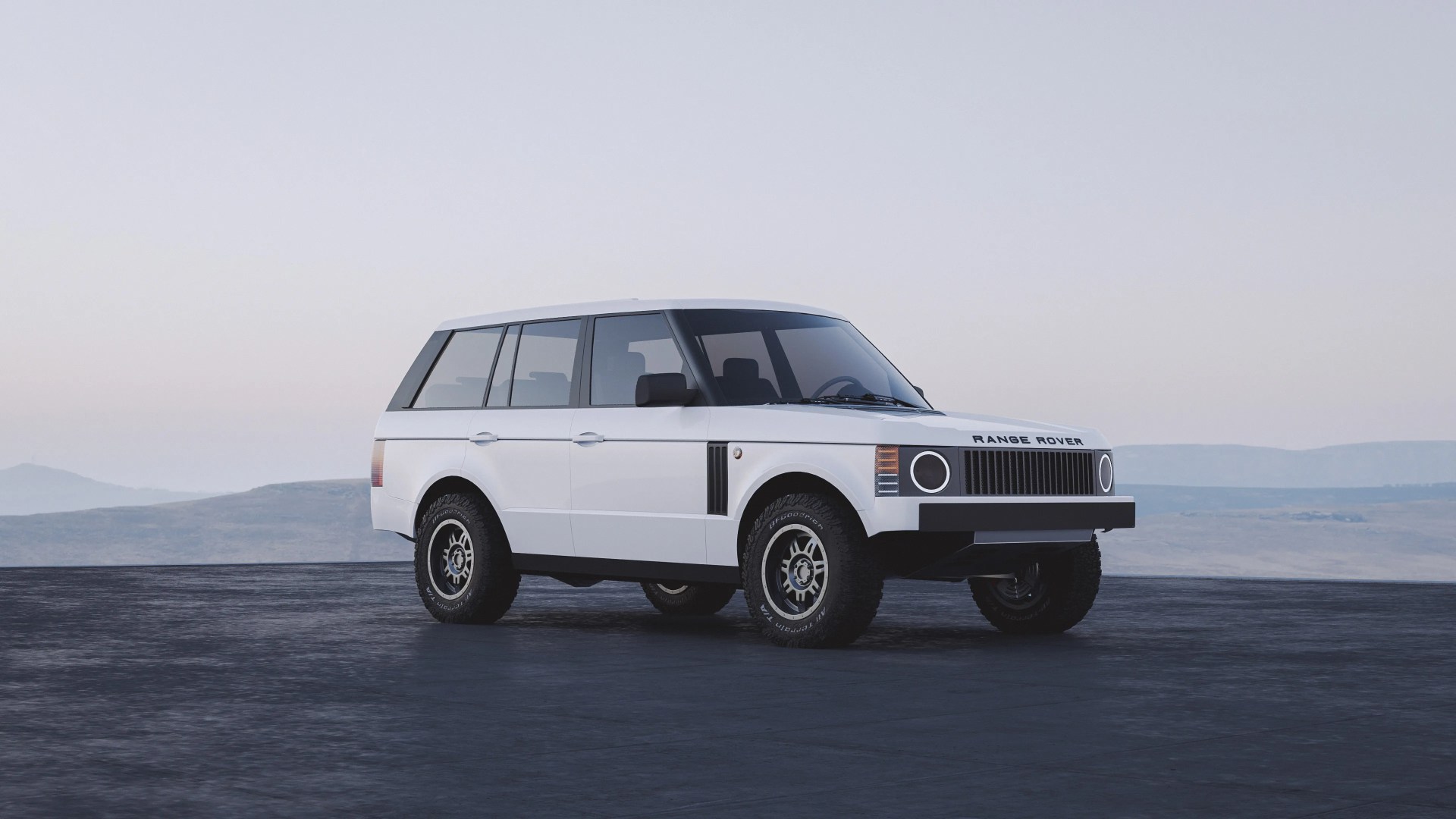 White Range Rover SUV with a boxy, classic design, black tinted windows, and off-road tires, parked on a dark paved surface with a mountainous landscape in the background under a clear sky.