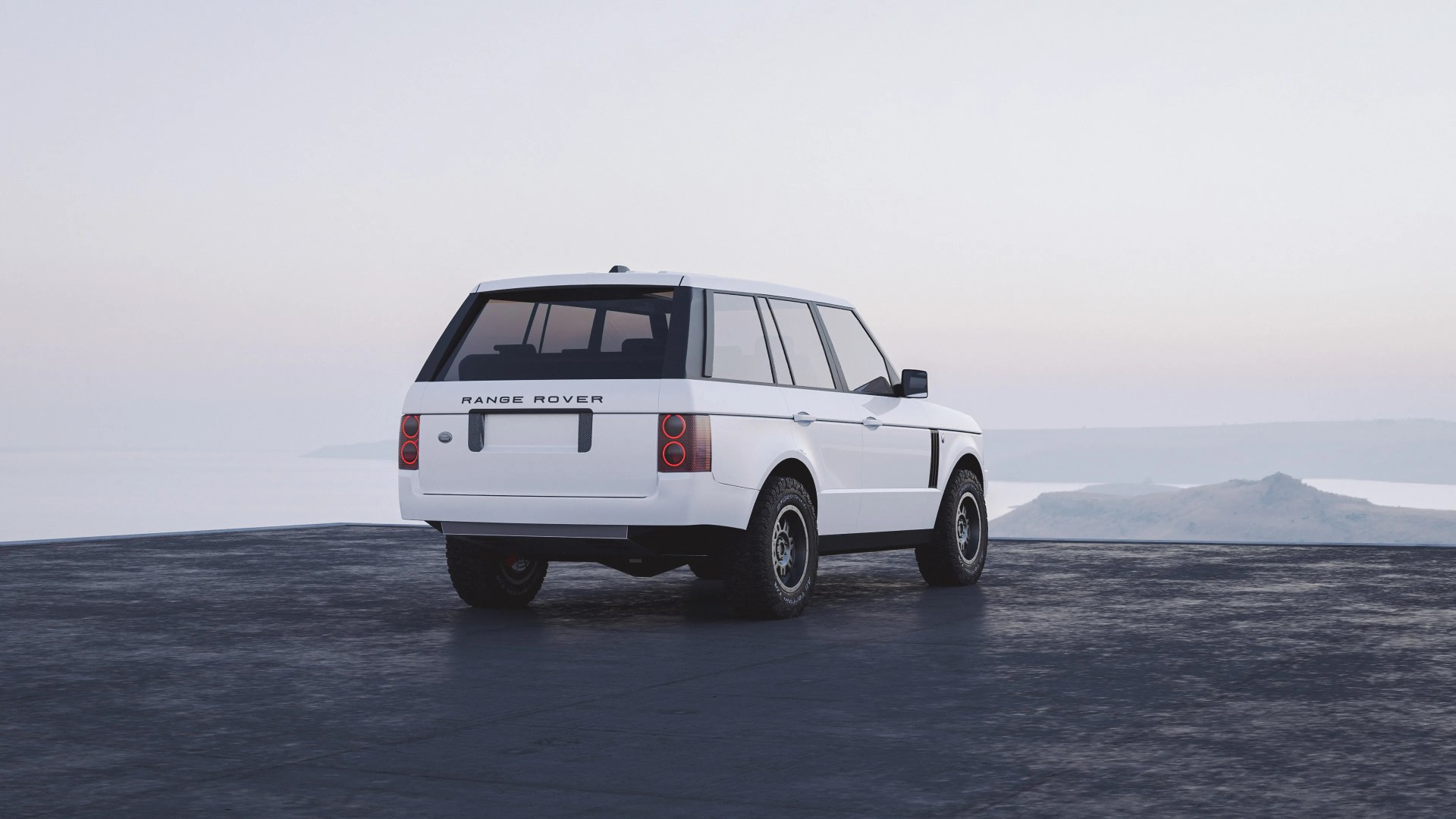 White Range Rover SUV viewed from the rear three-quarter angle, parked on a dark paved surface with a misty landscape and water in the background. The vehicle has tinted windows, round rear lights, and off-road tires.