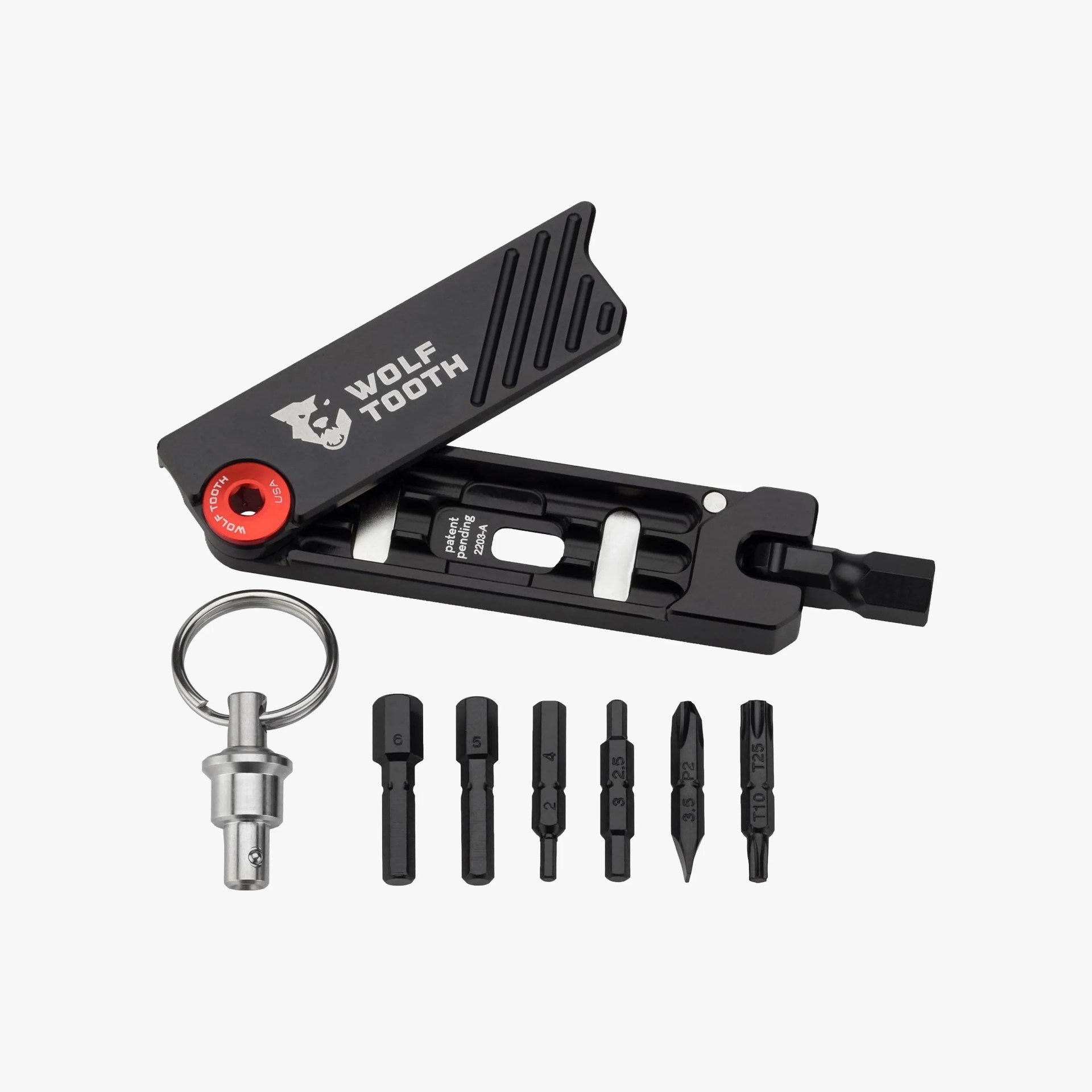 Compact black multi-tool with the brand name "Wolf Tooth" printed on the top cover. The tool is open, revealing a set of seven interchangeable bits arranged in a row below it, including hex, Phillips, and Torx bits. A silver keyring attachment is also included. The tool has a sleek, modern design with a red pivot point.