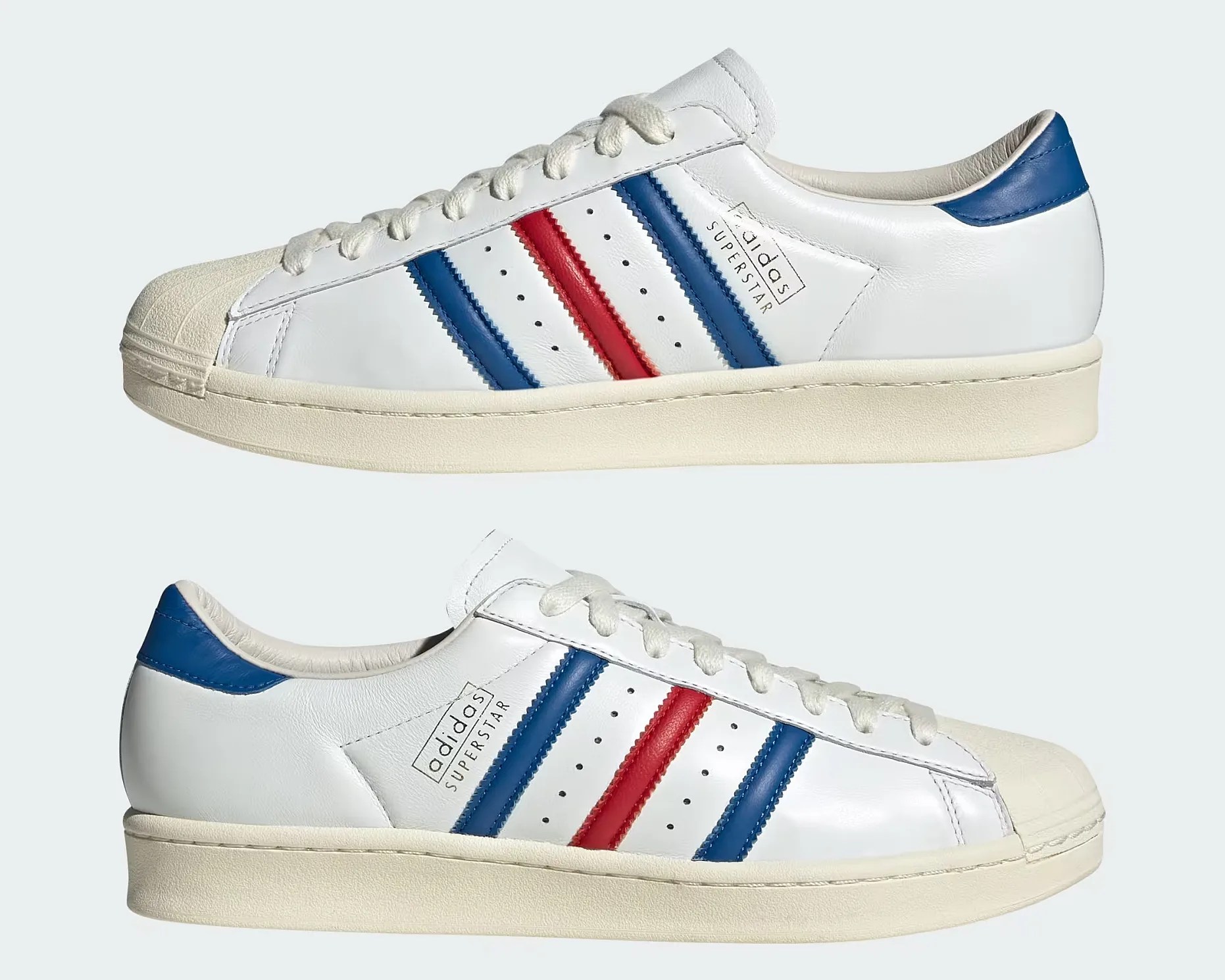 Pair of white Adidas Superstar sneakers with blue and red stripes on the sides, blue heel tabs, white laces, and off-white rubber soles and shell toes. The Adidas Superstar logo is printed near the stripes on the outer side of each shoe.