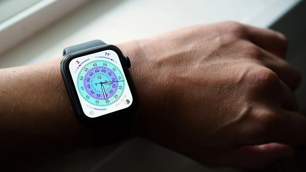 Smartwatch with a black band on a wrist, displaying a colorful circular dial with multiple concentric rings showing hours, minutes, and seconds, along with temperature (71°F) and UV index (3) indicators.