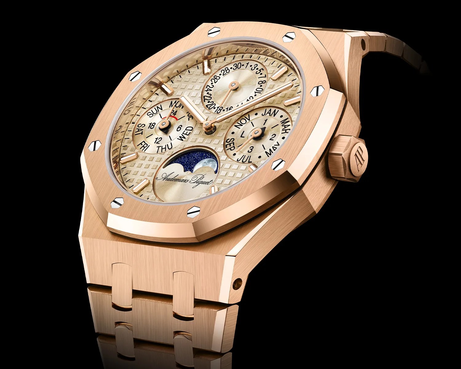 Rose gold luxury wristwatch with an octagonal bezel secured by eight screws. The dial features a textured pattern with three subdials displaying the day, date, and month, along with a moon phase indicator at the bottom. The watch hands and hour markers are also rose gold, and the crown is engraved with the initials "AP." The bracelet is made of matching rose gold links.