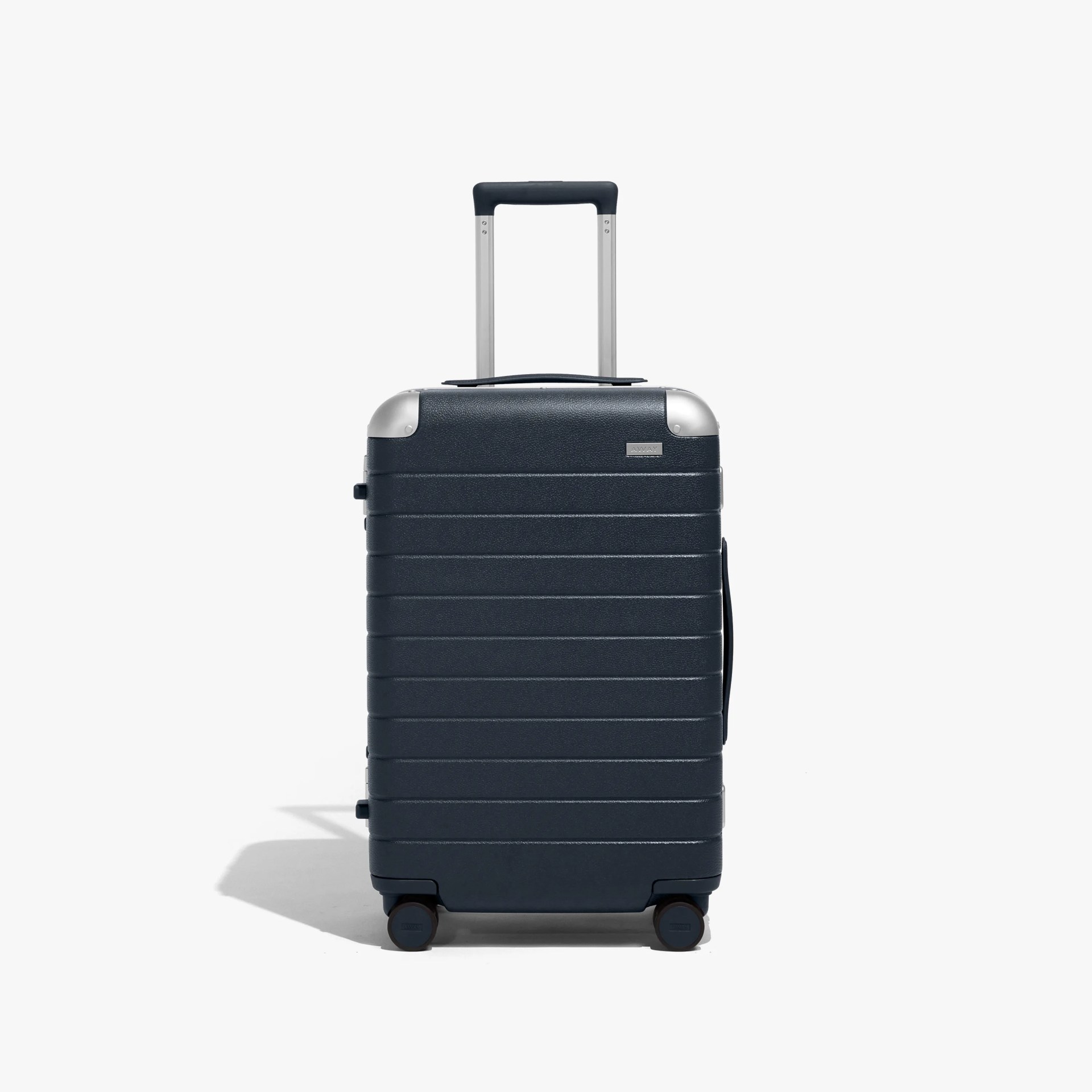 Dark gray hard-shell suitcase with horizontal ridges, silver corner protectors, and a retractable handle. It has four wheels and a side handle for carrying.