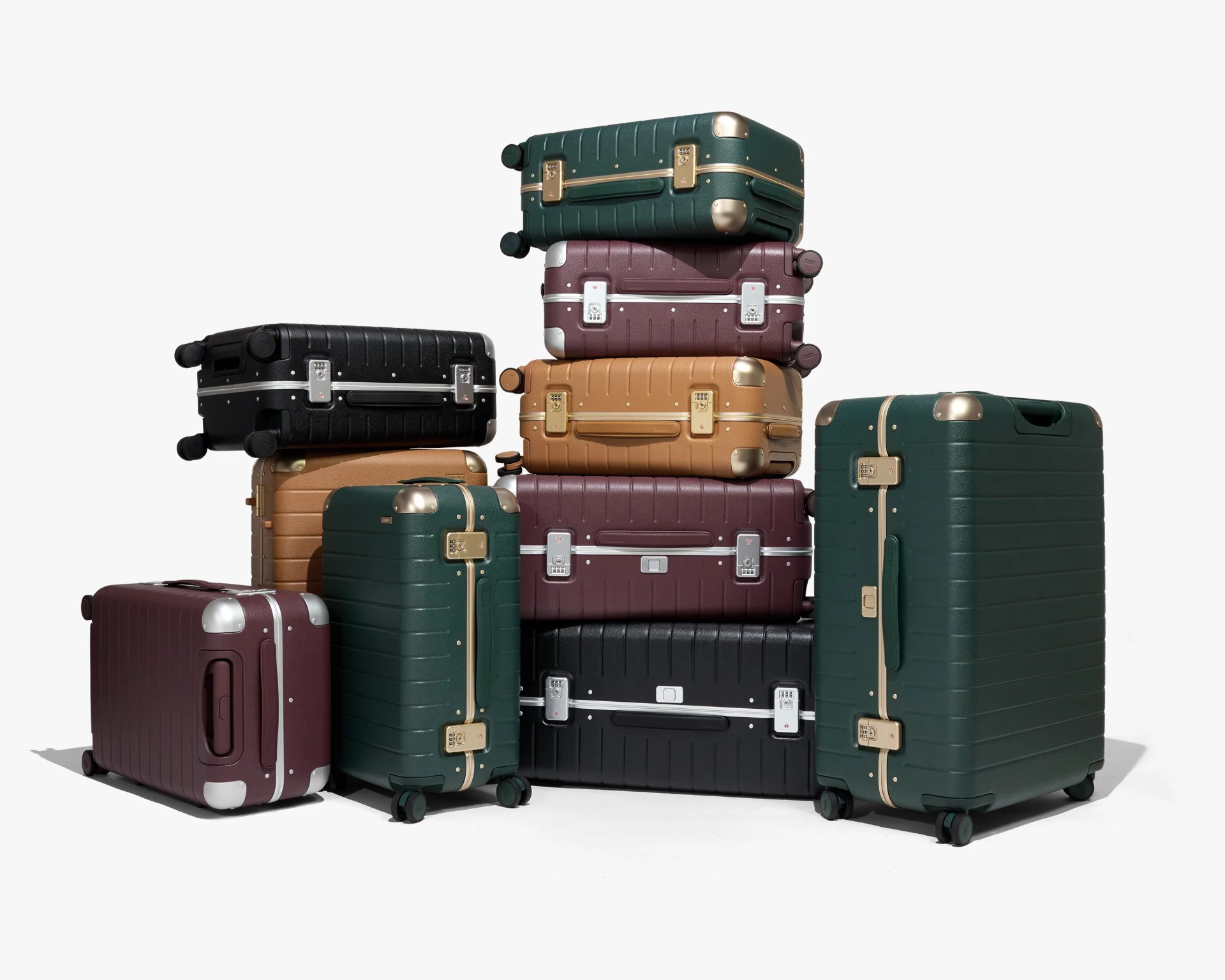 A collection of hard-shell suitcases in various sizes and colors, including dark green, maroon, black, and tan. The suitcases feature metallic corner protectors and combination locks, with some having gold accents and others silver. They are stacked and arranged in a pyramid-like formation on a white background.