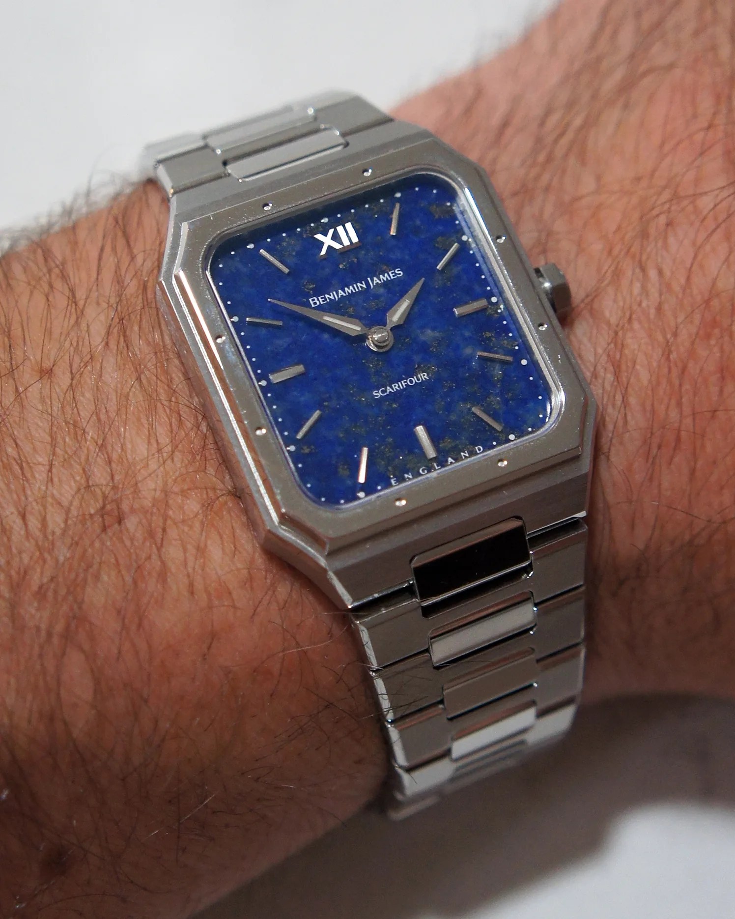 Silver metal wristwatch with a rectangular case and a deep blue speckled dial. The dial features silver hour markers and hands, with the brand name "BENJAMIN JAMES" and model name "SCARIFOUR" printed on it. The watch is worn on a wrist with a silver metal link bracelet.