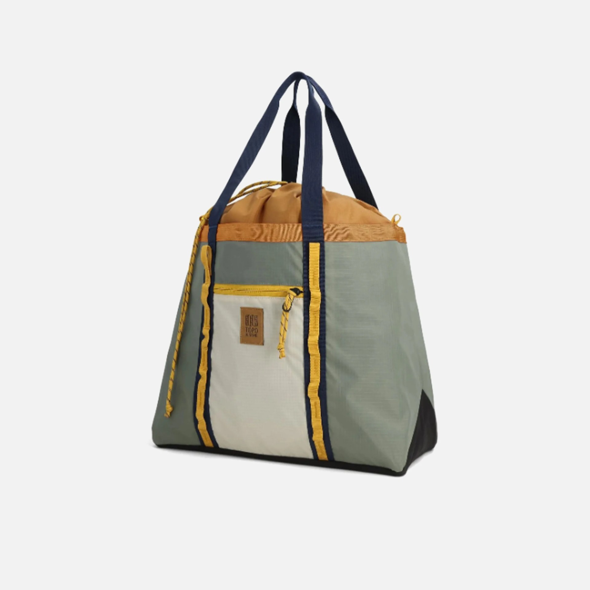 A multi-colored tote bag with a triangular shape, featuring a light green body, a tan top section with a drawstring closure, and a front pocket in off-white with a yellow zipper. The bag has navy blue handles and yellow trim accents along the front pocket and handles. There is a small brown patch with text on the front pocket.